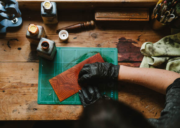 Gemma ahand dyeing a piece of leather for a hip flask, the design showcases some topographic lines across the leather.