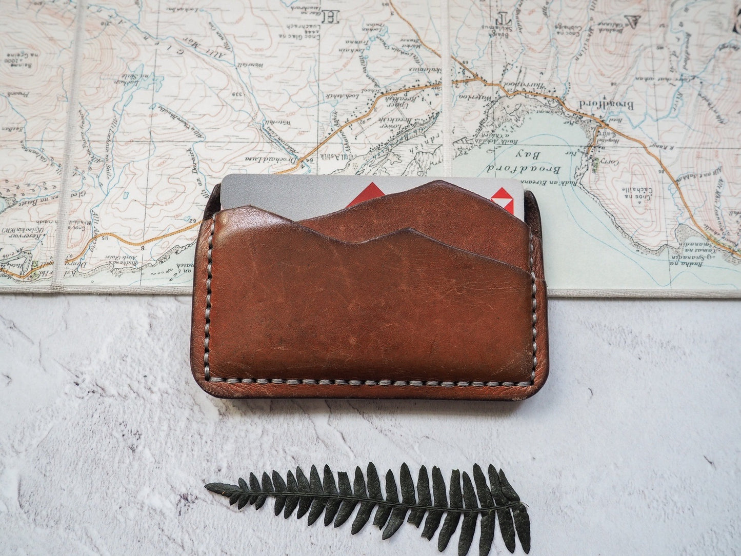 A five year old card holder , in medium brown dye with grey stitch. This piece is the prototype of our original mountain card holder.