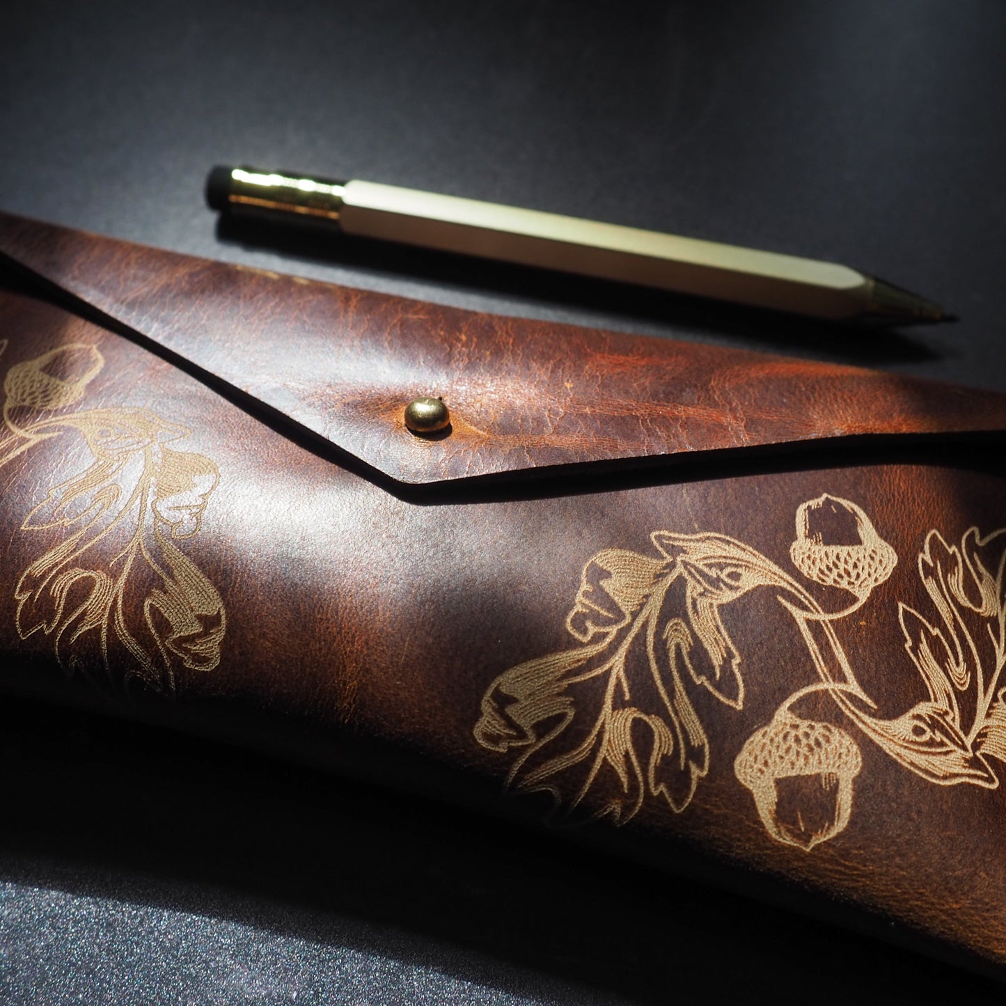 Brown leather pouch with floral embossing and a pen on a dark surface