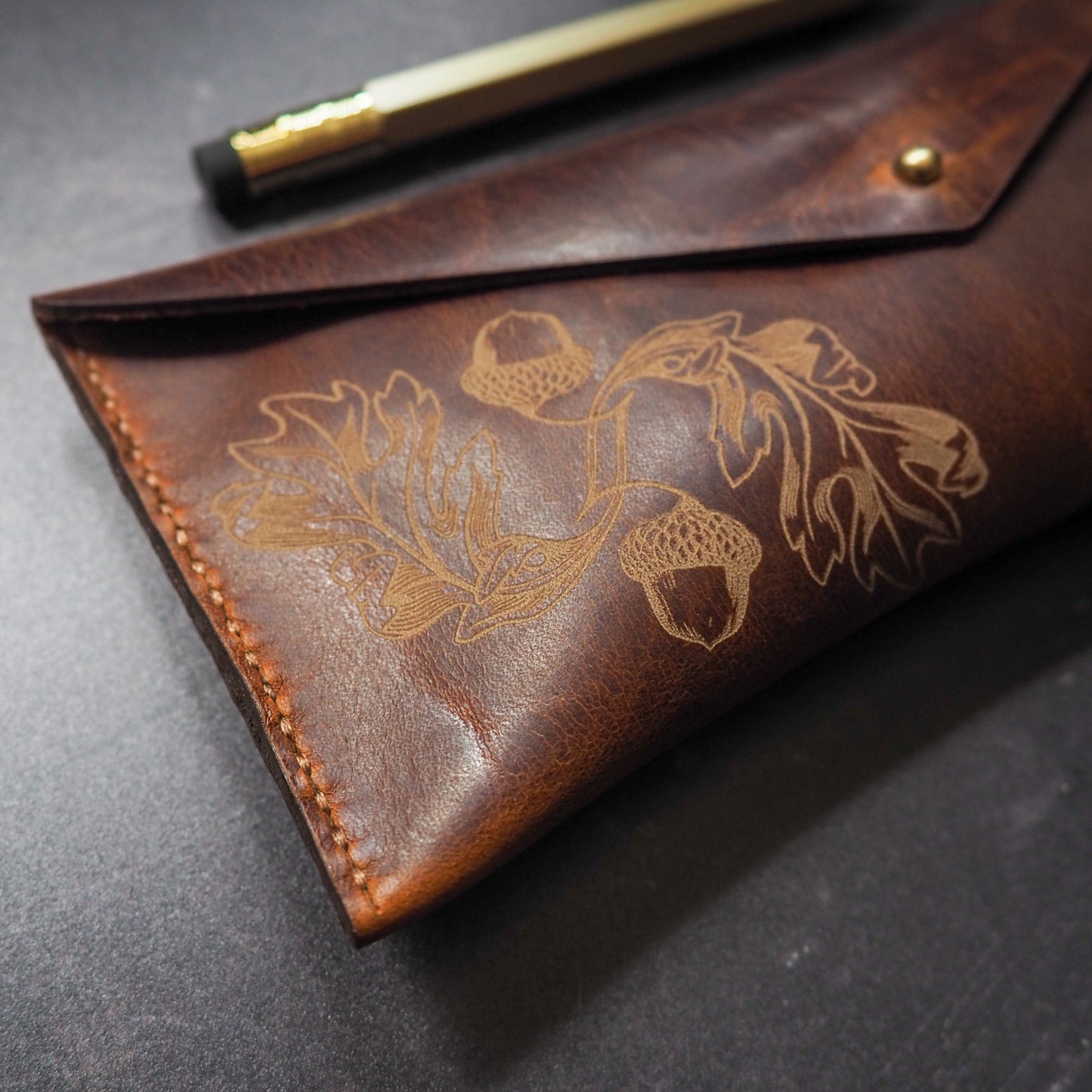 Brown leather pouch with oak leaf and acorn design on a dark surface