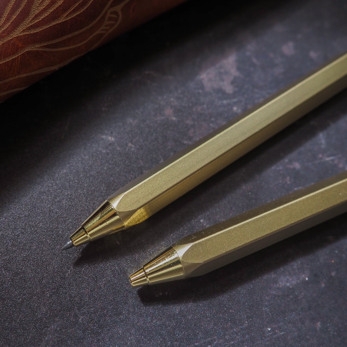 Two gold pencils on a dark textured surface