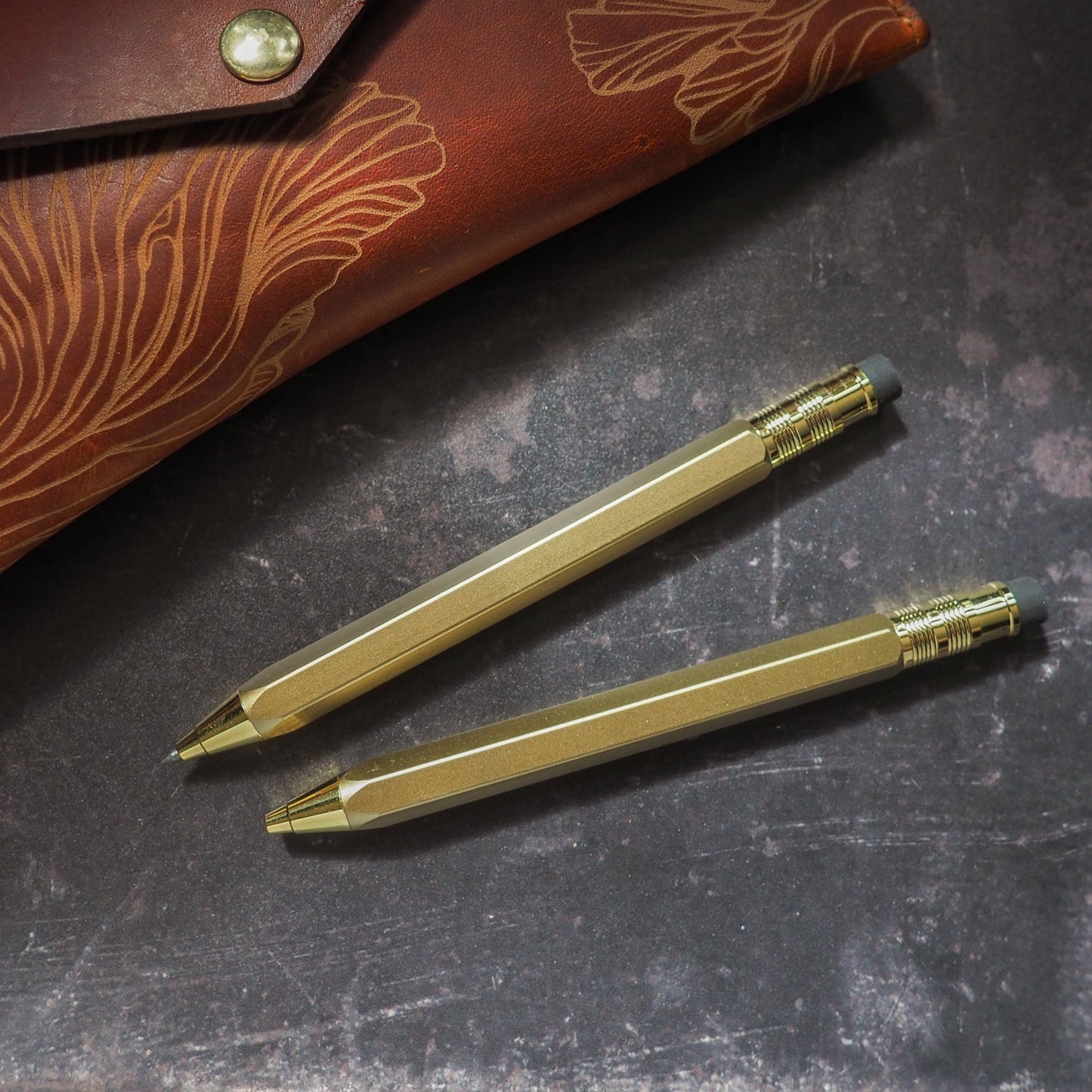 Two gold pens with a leather case on a dark surface
