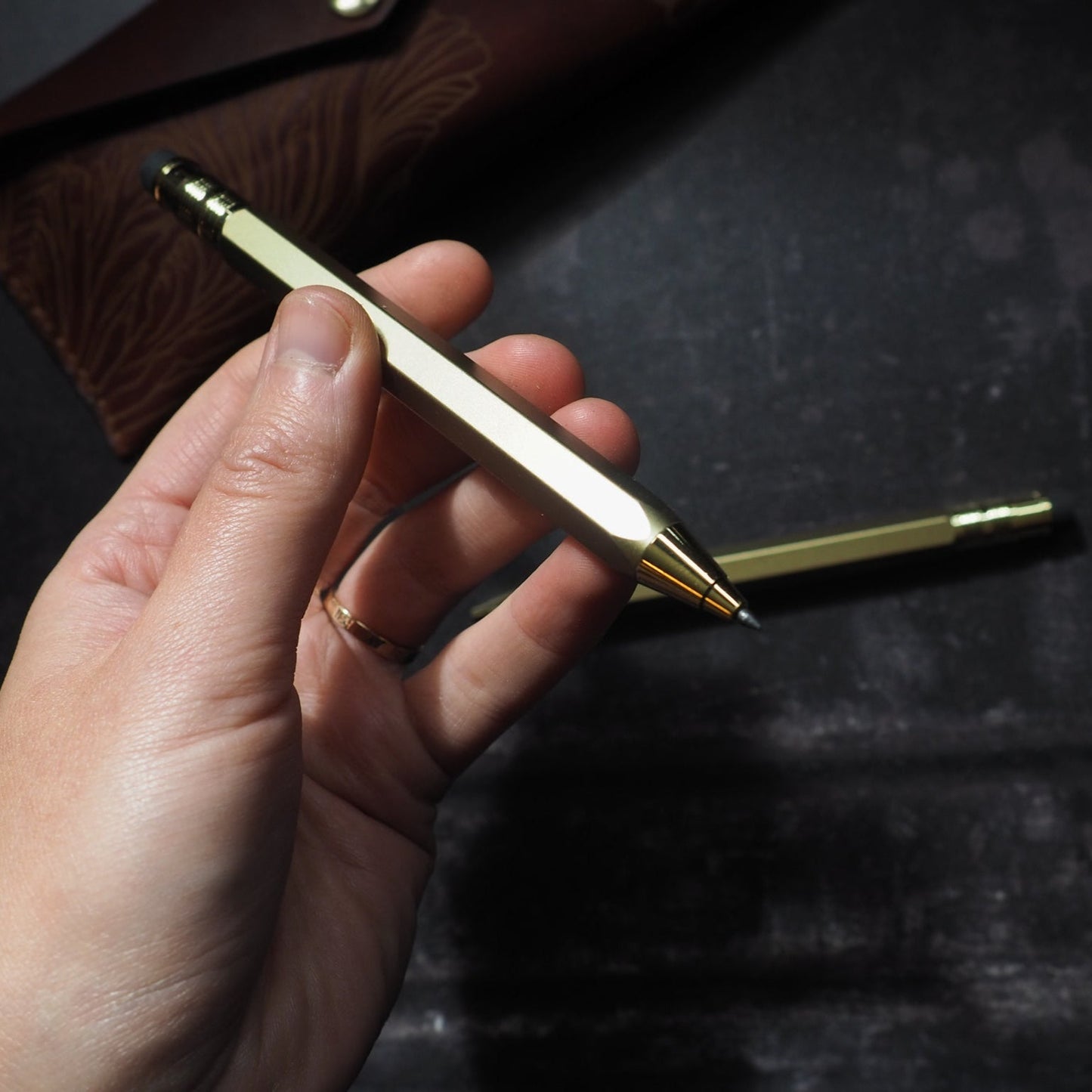 Hand holding a gold mechanical pencil against a dark background
