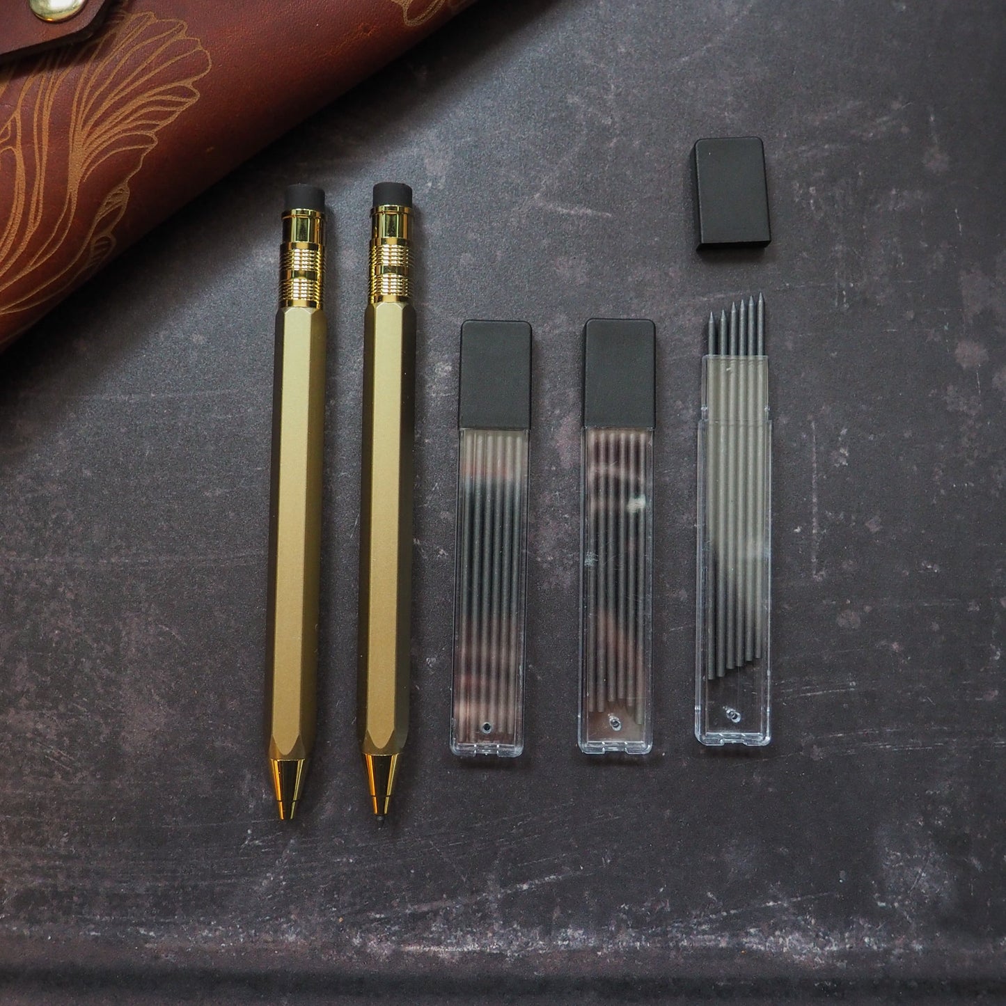 Two gold pencils and their refills on a dark surface