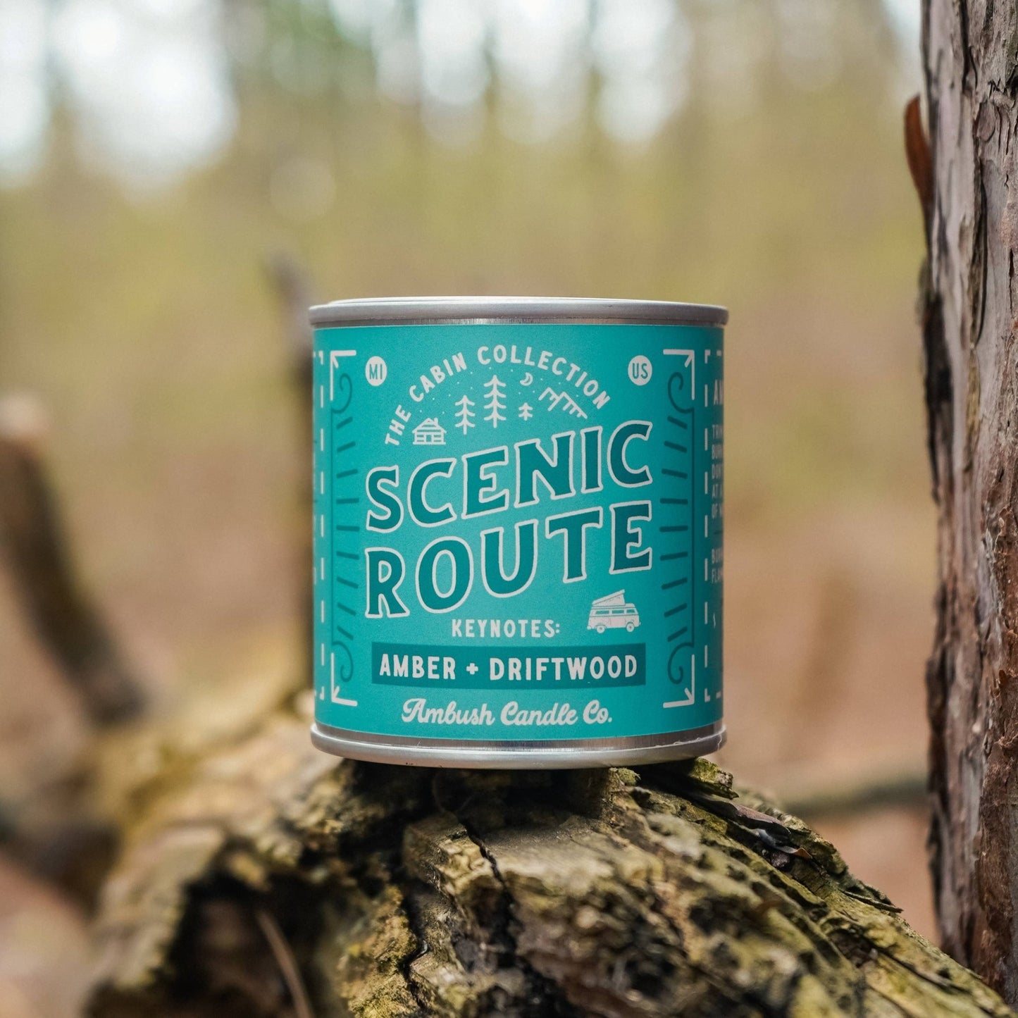 A can of Scenic Route amber + driftwood soy candle by Ambush Candle Co. placed on a wooden surface with a natural background.
