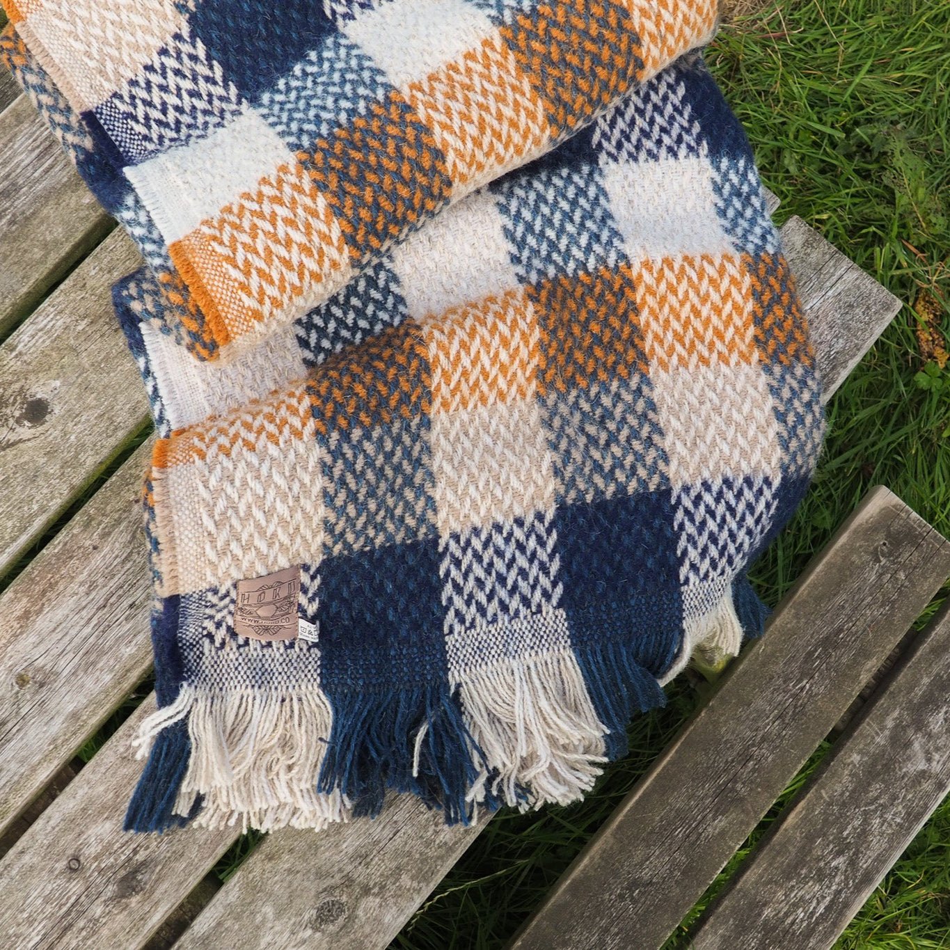Plaid blanket with blue, mustard yellow, and beige celtic pattern on a wooden bench outdoors.