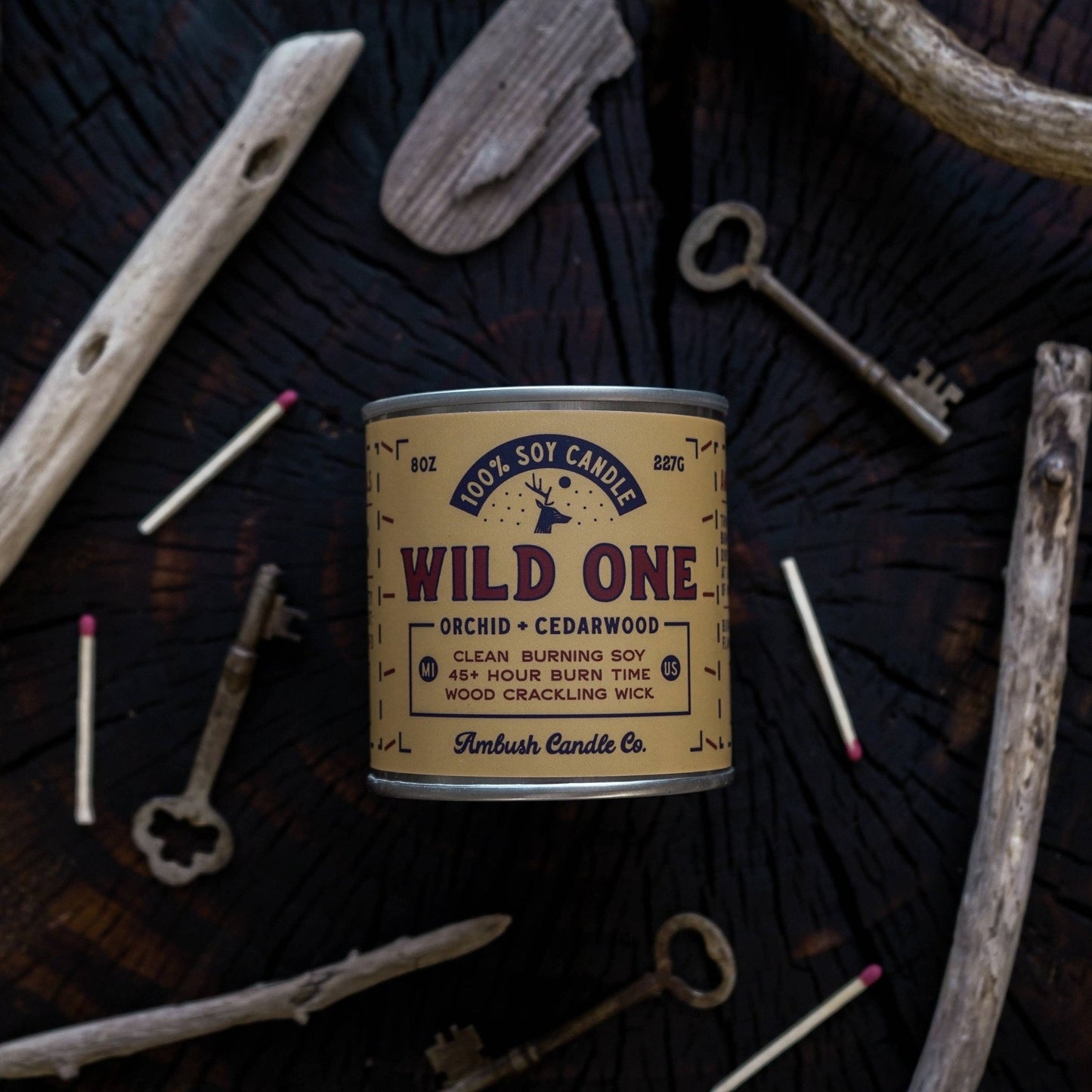 An 8oz soy candle with 'Wild One' labeled, placed on a wooden surface surrounded by keys and a broken piece of a wooden object, indicating a rustic or outdoor theme.