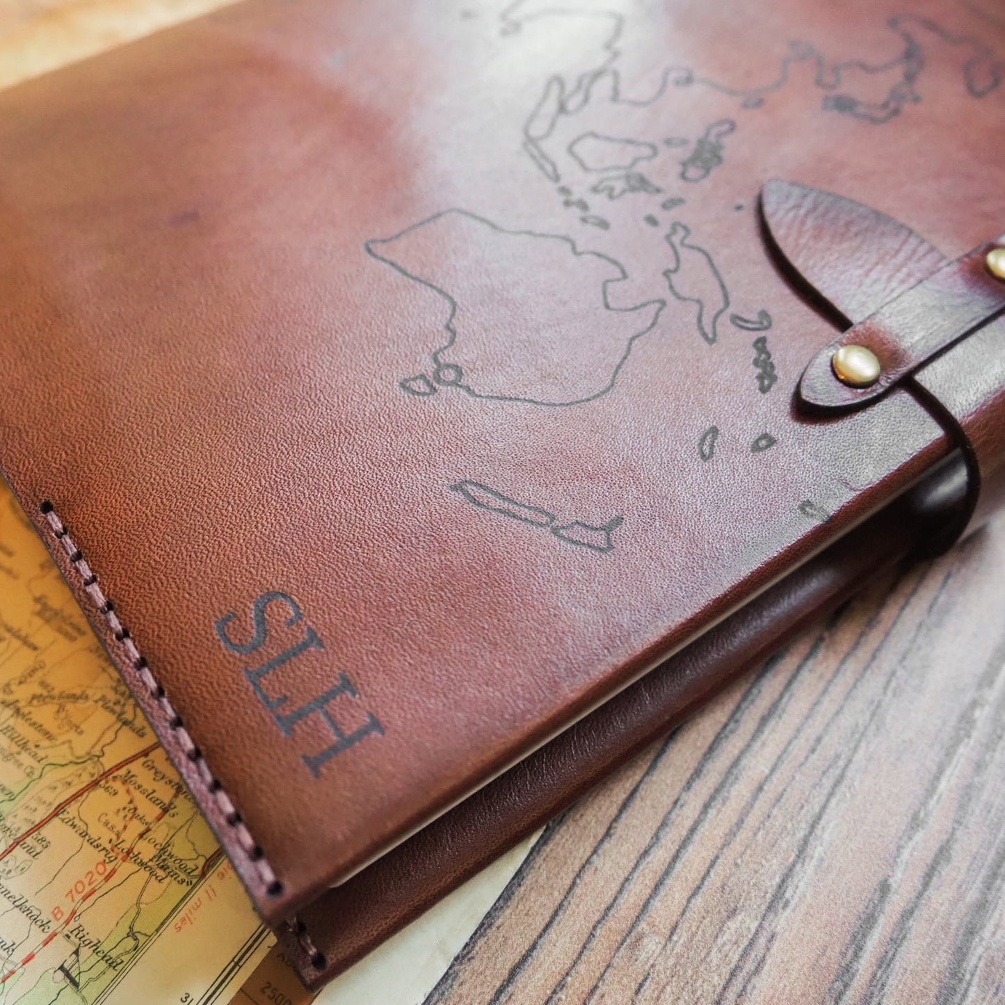 Brown leather notebook with engraved initial monogram and world map design on a wooden surface