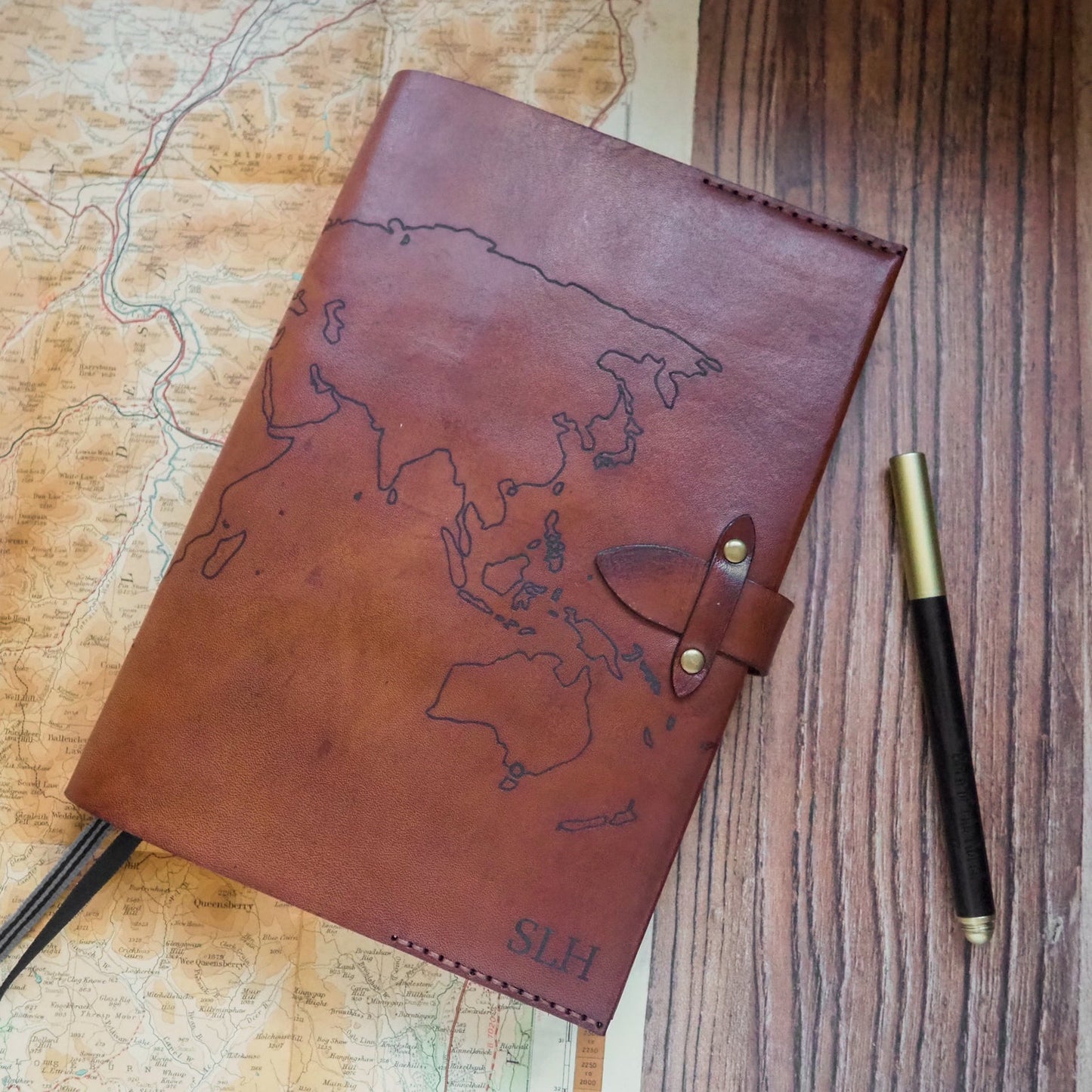 Brown leather notebook with world map design on a wooden surface with a pen.