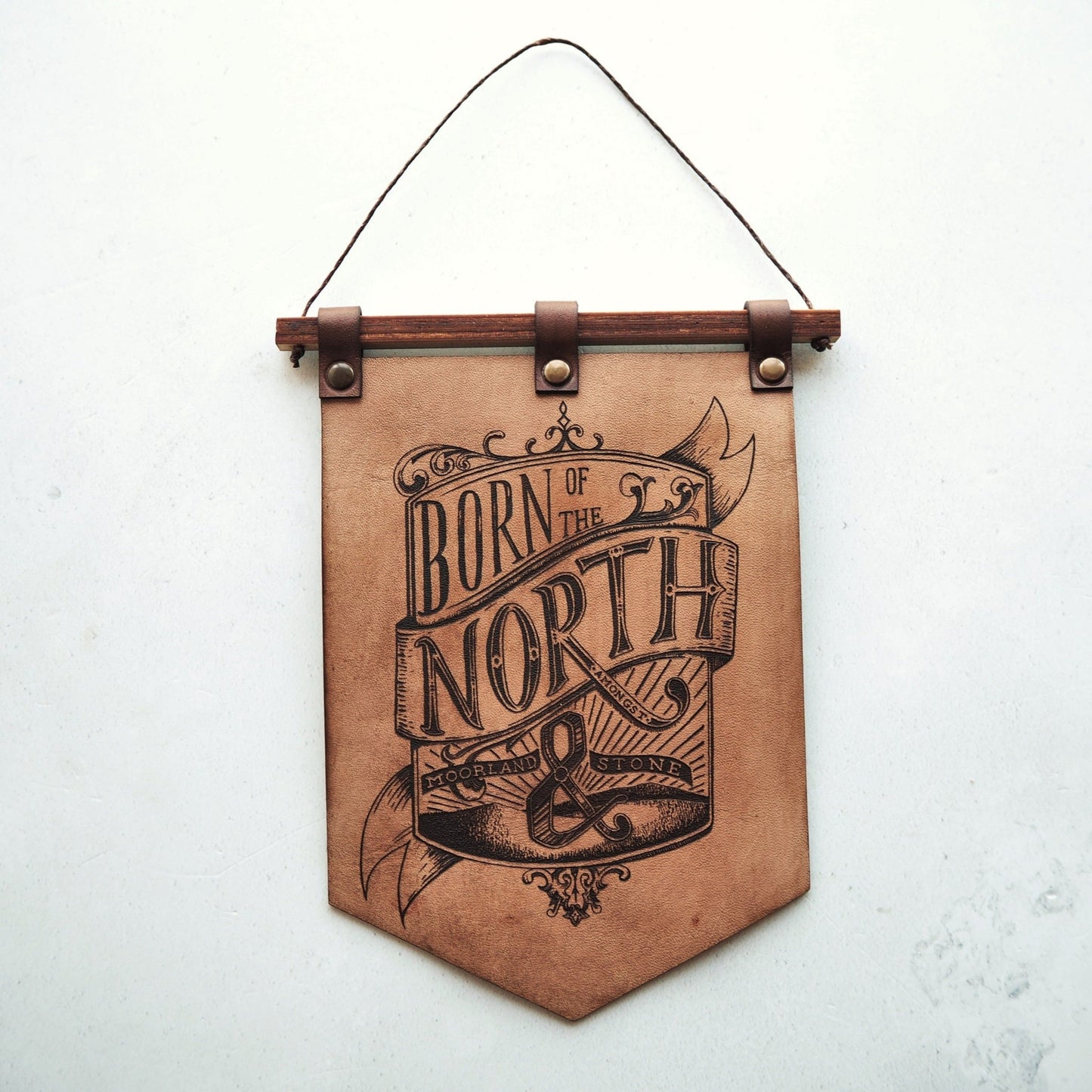 Born of the North banner made from hand dyed leather, a threaded wooden rail holds a leather banner which is engraved with an opulent crest style illustration containing the words
