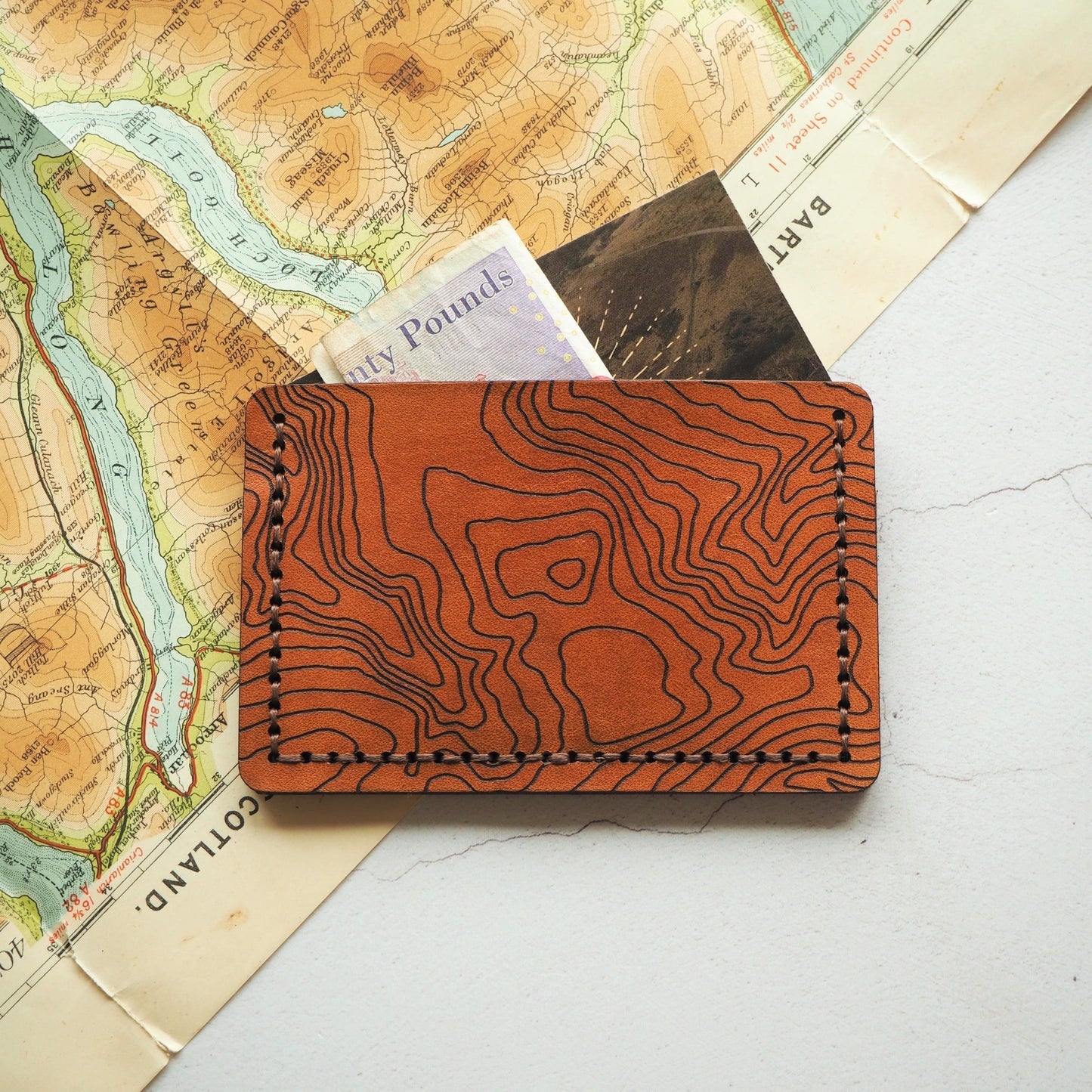 The engraved leather card holder with custom topography with cash and cards stored safely.