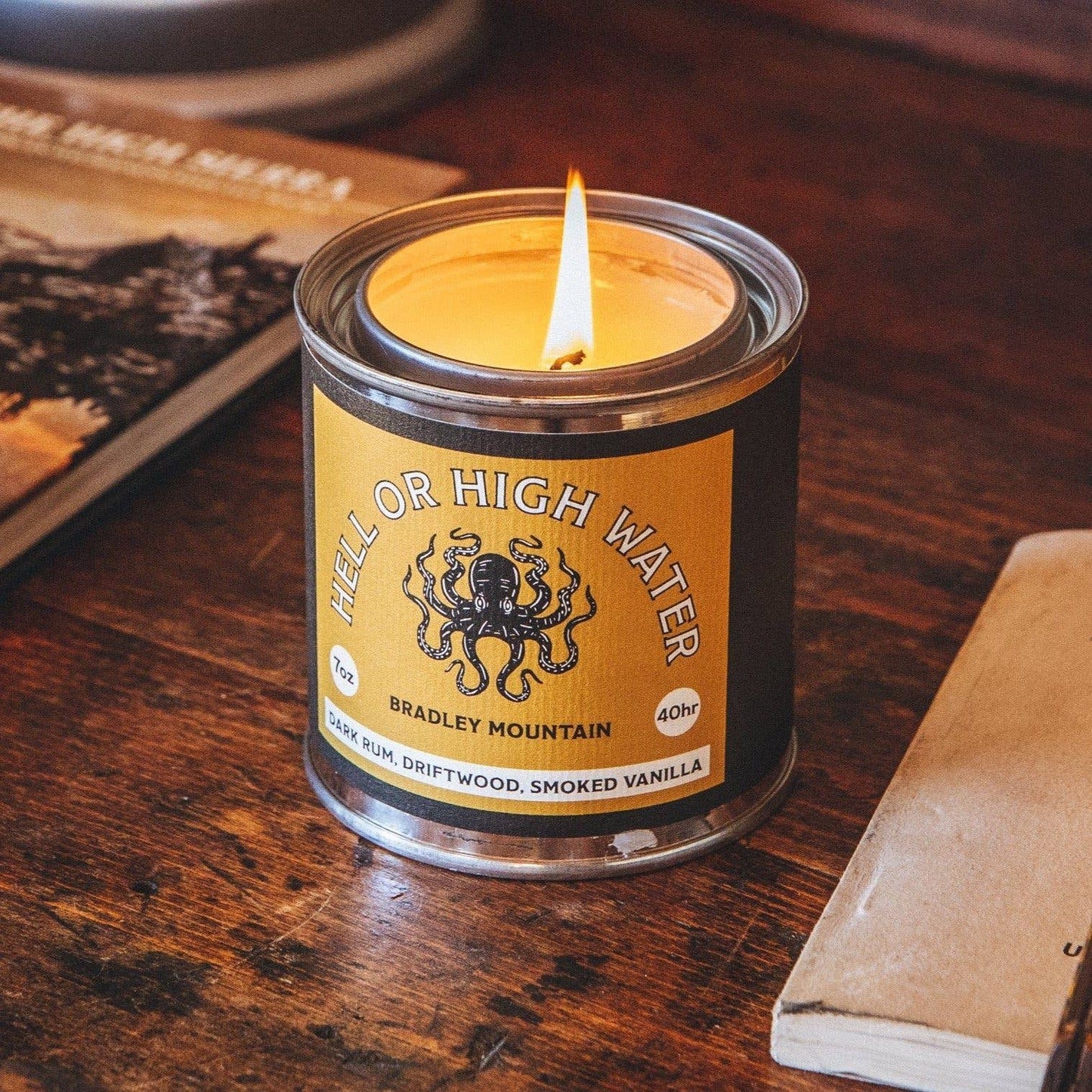 The Hell or High Water Candle, lit and standing on an old oak table.