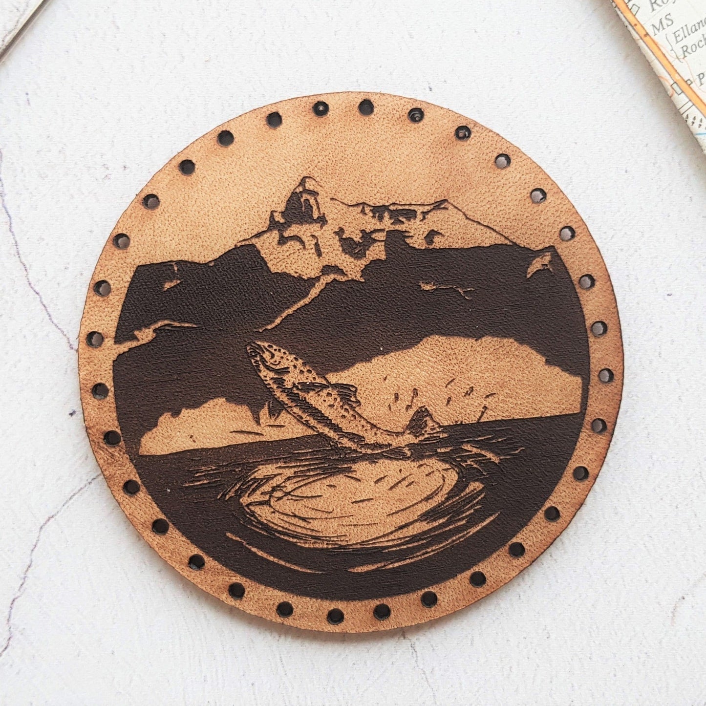 The Fishing patch by HORD - This leather patch is hand dyed and engraved with a majestic fish jumping out of a mountain lake. Perfect stocking fillers or gifts for lovers of the outdoors, fishing, hunting and hiking.