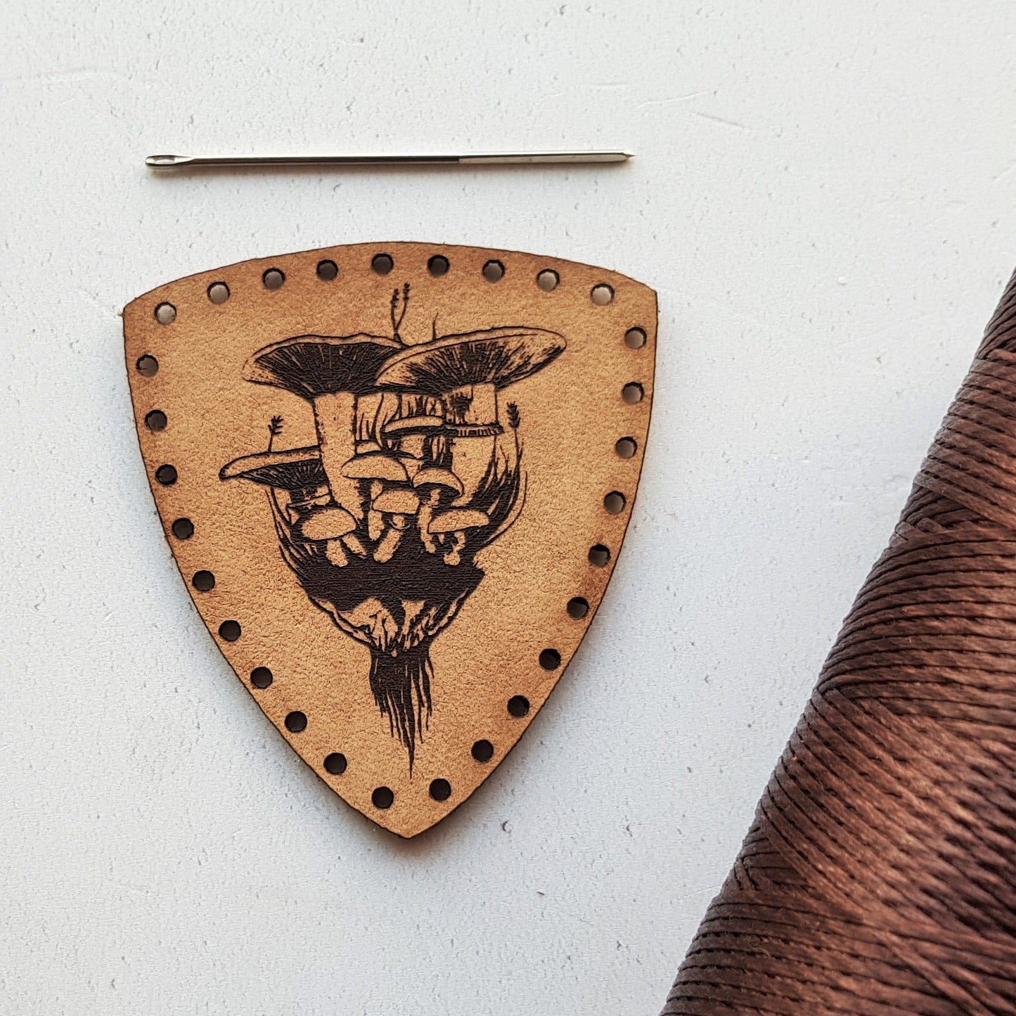 This shield shaped leather patch is engraved with a bunch of wild fungus pulled from the earth on a foraging expedition. Pre-cut patch holes make this easy to stitch onto your foraging bag. The mushroom patch from Hord.