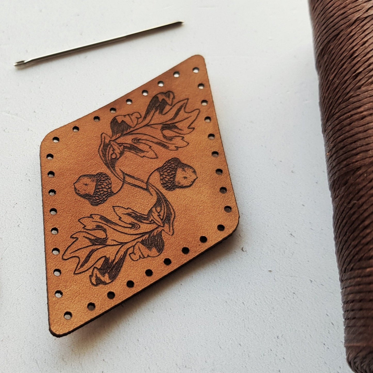 A pattern of acorns and oak leaves is engraved onto this diamond shaped patch, hand dyed a light brown and with stitch holes to make sewing super easy. The Oak Leaf Patch from Hord.