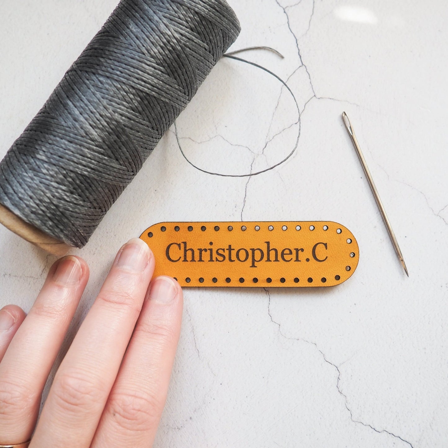 The personalised leather patch by hord. A yellow leather patch engraved with the name Christopher. C, in a classic font Cambria. The patch is shaped like a long oval.
