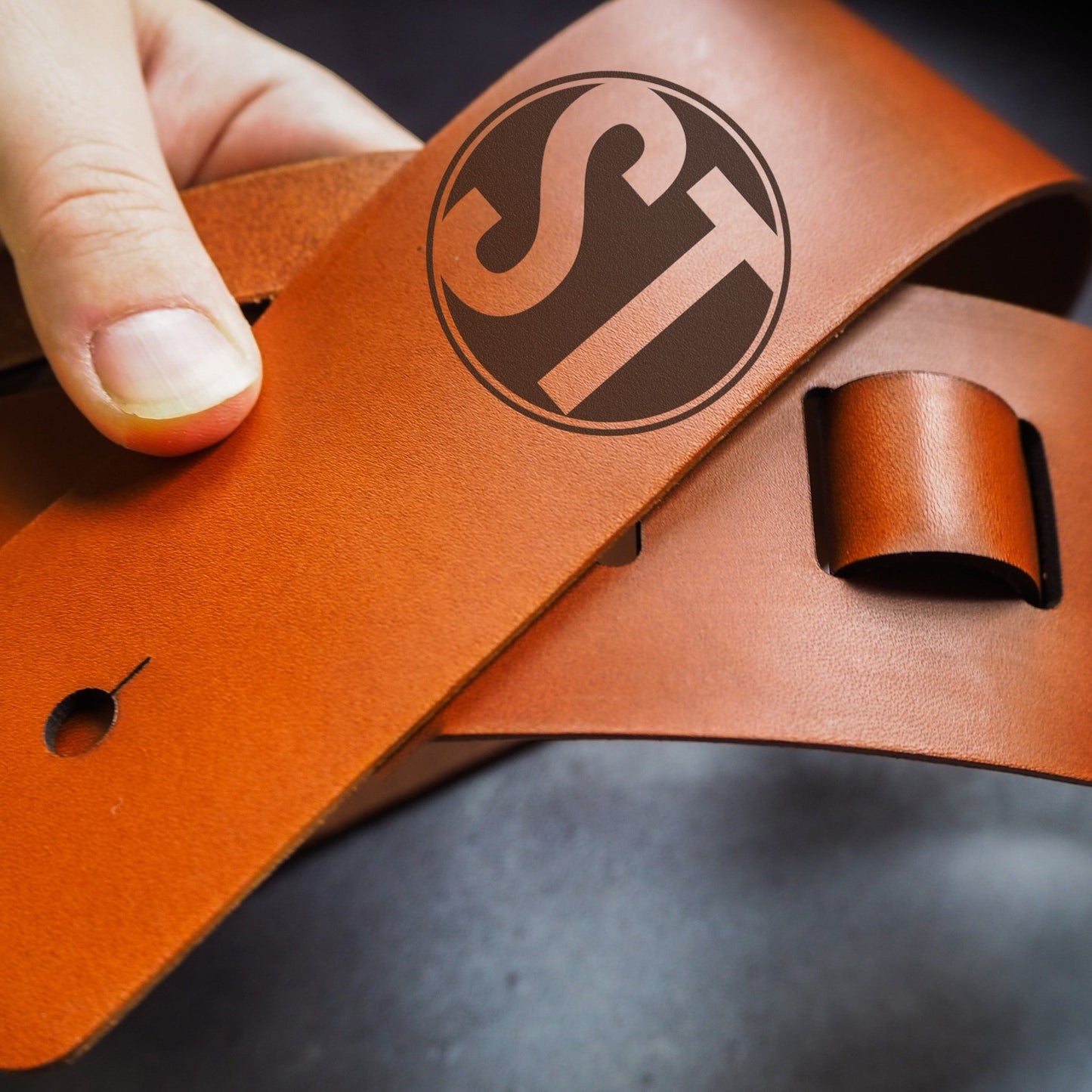 Custom logo on a tan thick leather guitar strap.