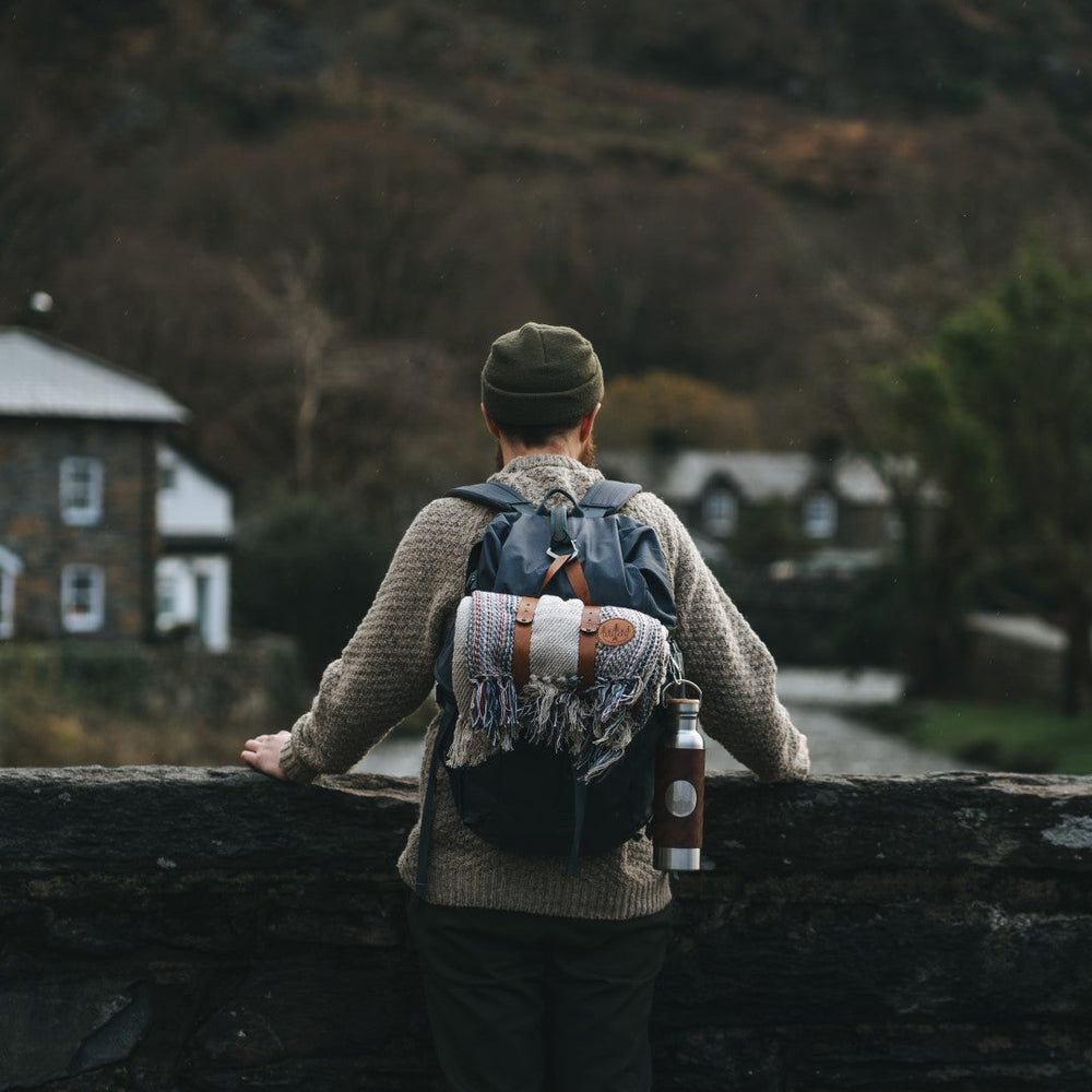 A man stood on a bridge in Wales wearing a HORD beanie and carrying a HORD blanket and adventure bottle.