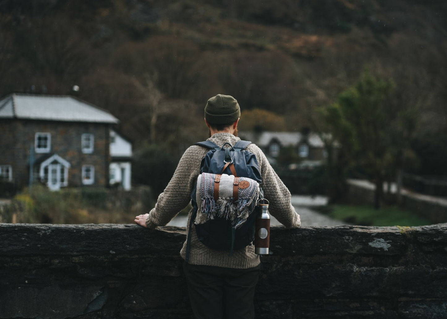 A man stood on a bridge in Wales wearing a HORD beanie and carrying a HORD blanket and adventure bottle.