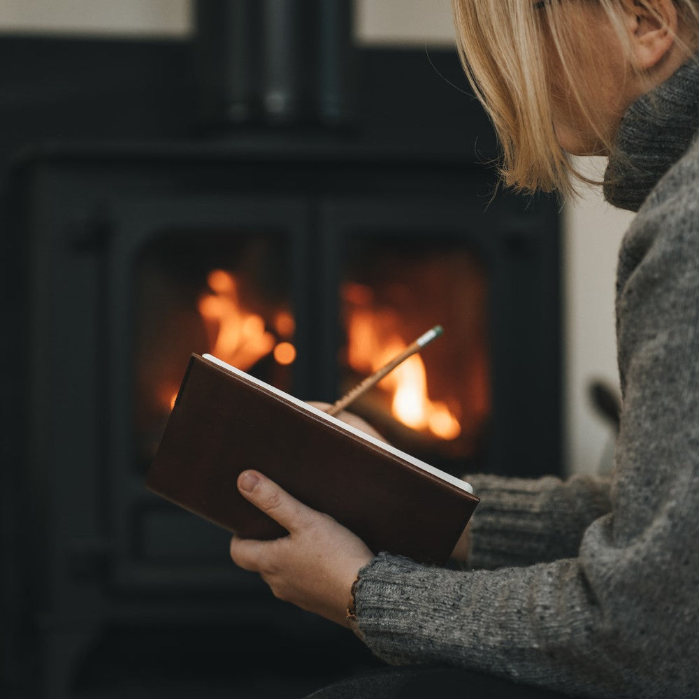 a woman sits by a stove writing in her journal