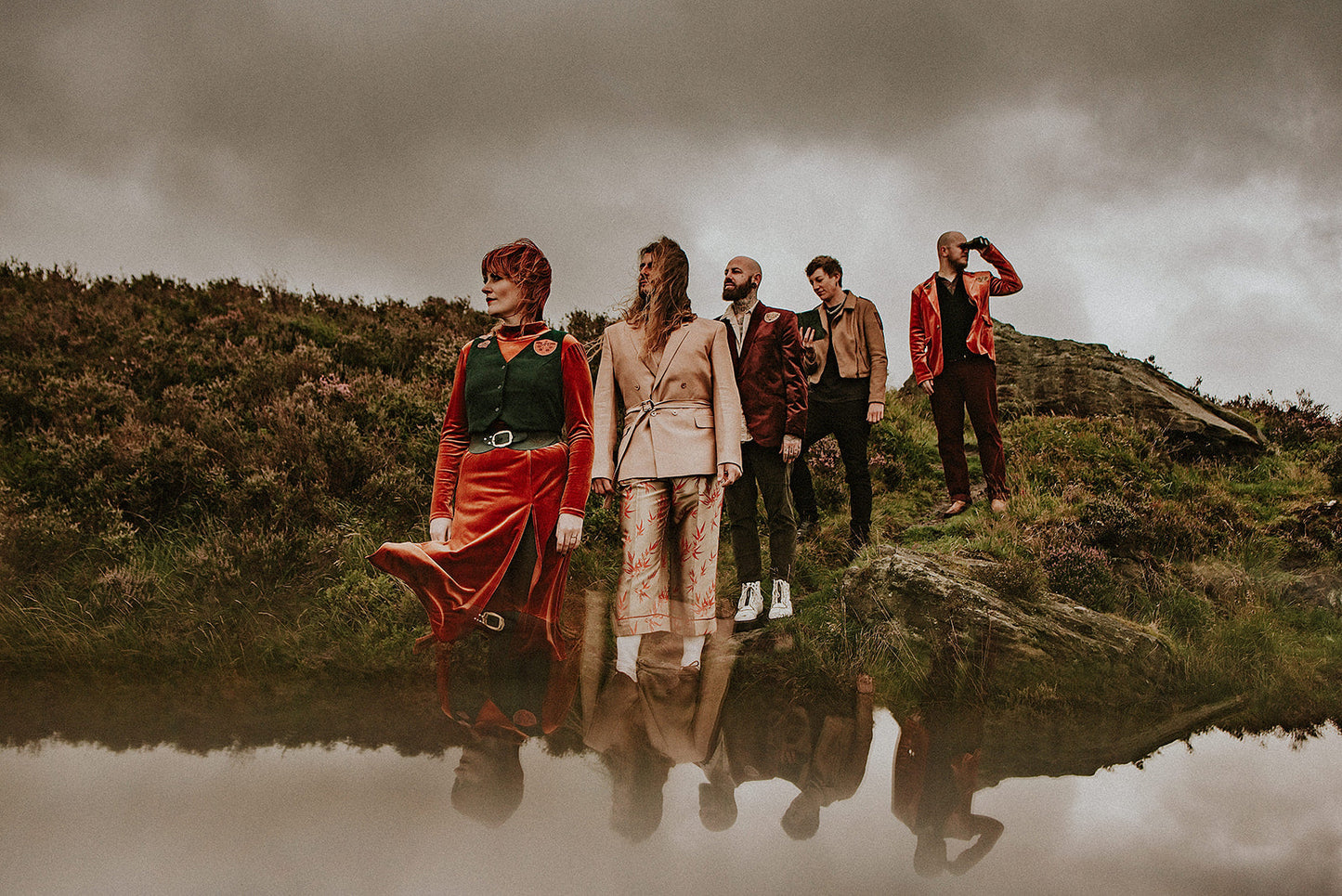 five people stood on the Yorkshire moors of marsden wearing orange and green psychedelic accessories made from leather. The photograph has multiple exposure, reflecting the sky at the bottom