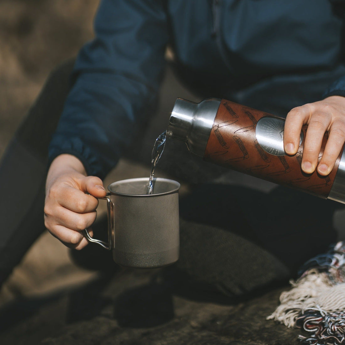 A woman pours hot water from her insulated scout adventure bottle into a steel camping cup, by Hord