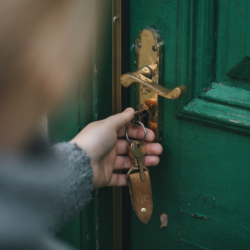  A woman unlocking her door with our Rof Key Fob engraved with the initials EJC in cambria. The fob is made from our sand coloured soft pull-up leather.