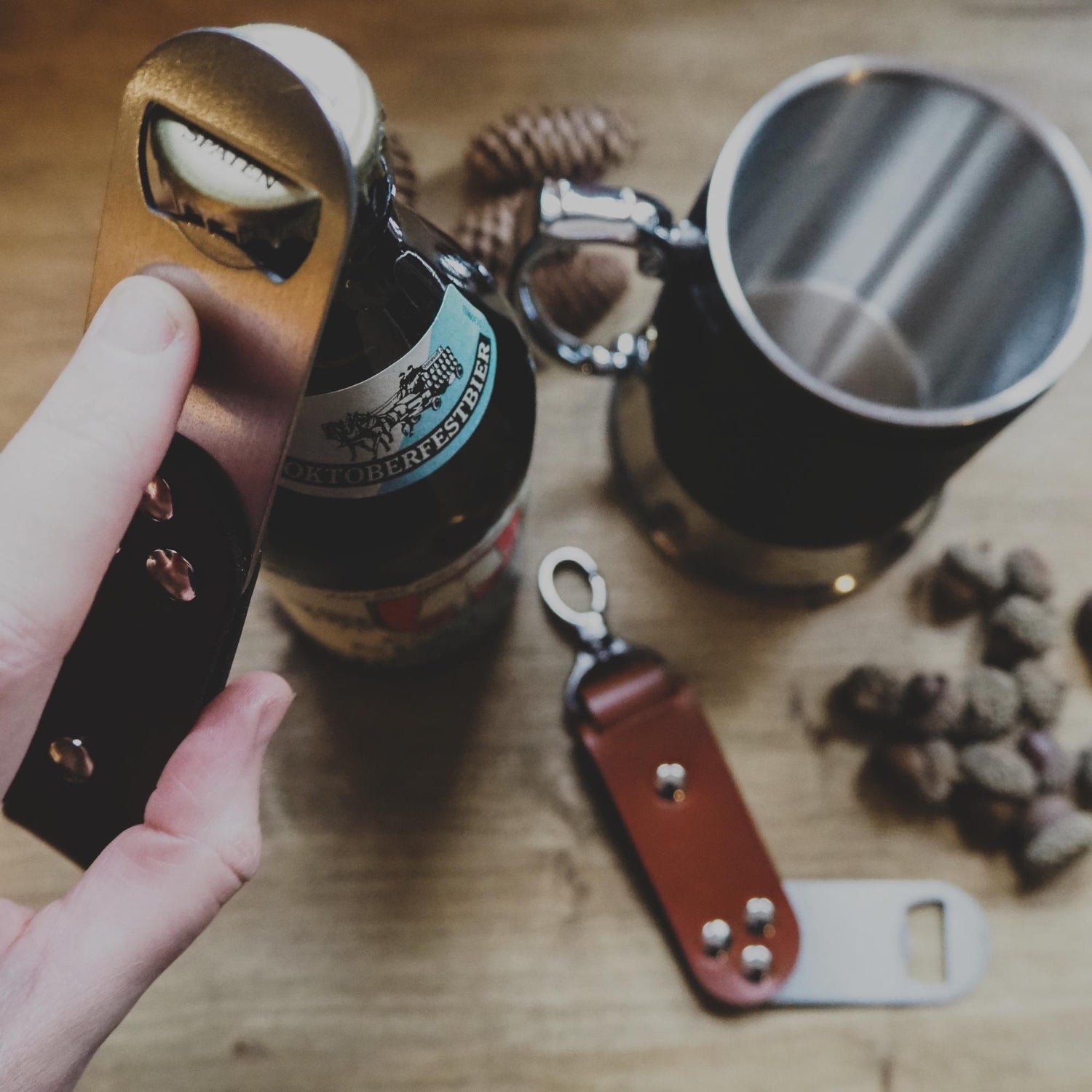A swivel bottle opener by hord being used to open a bottle of beer, next to a hord leather wrapped tankard.