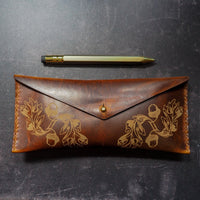Brown leather pouch with floral embossing on a dark surface