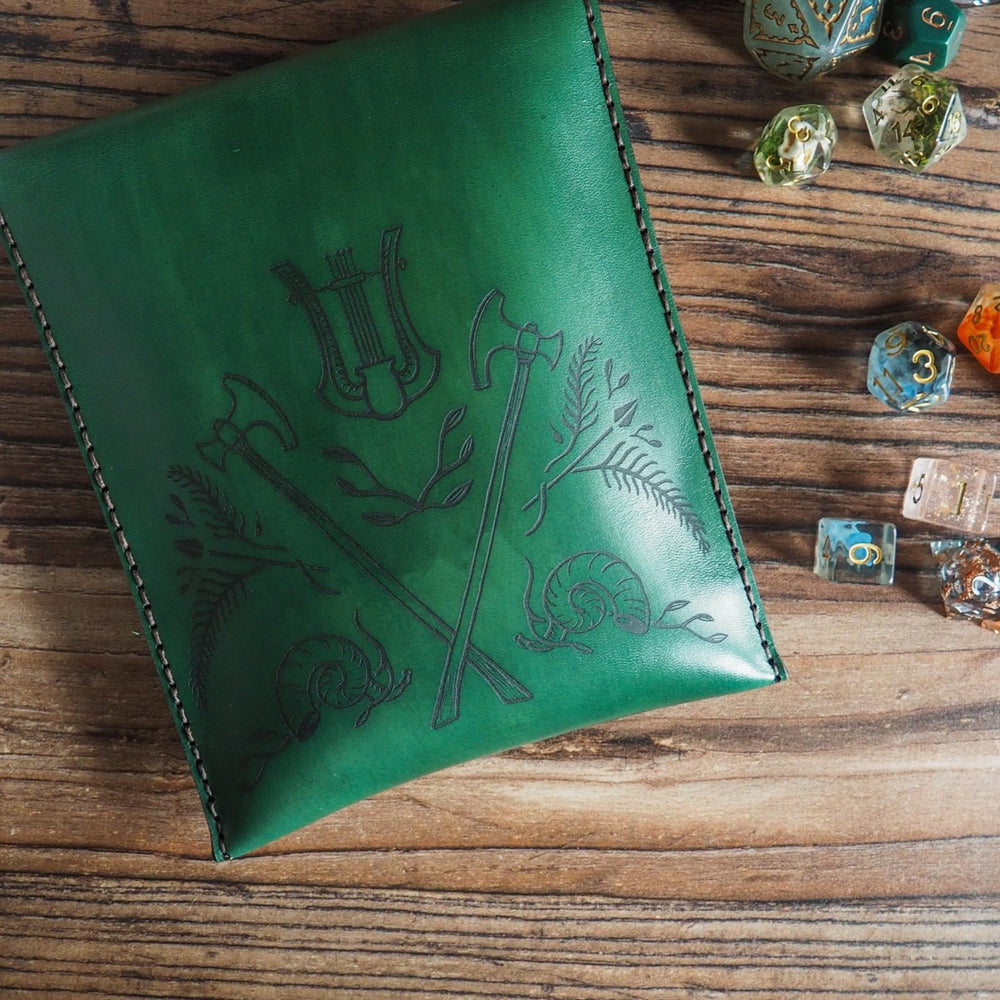 
                  
                    Green leather pouch with engraved design on a wooden surface with dice around it
                  
                