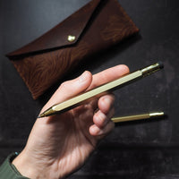 Hand holding a gold pen with a brown leather case on a dark background