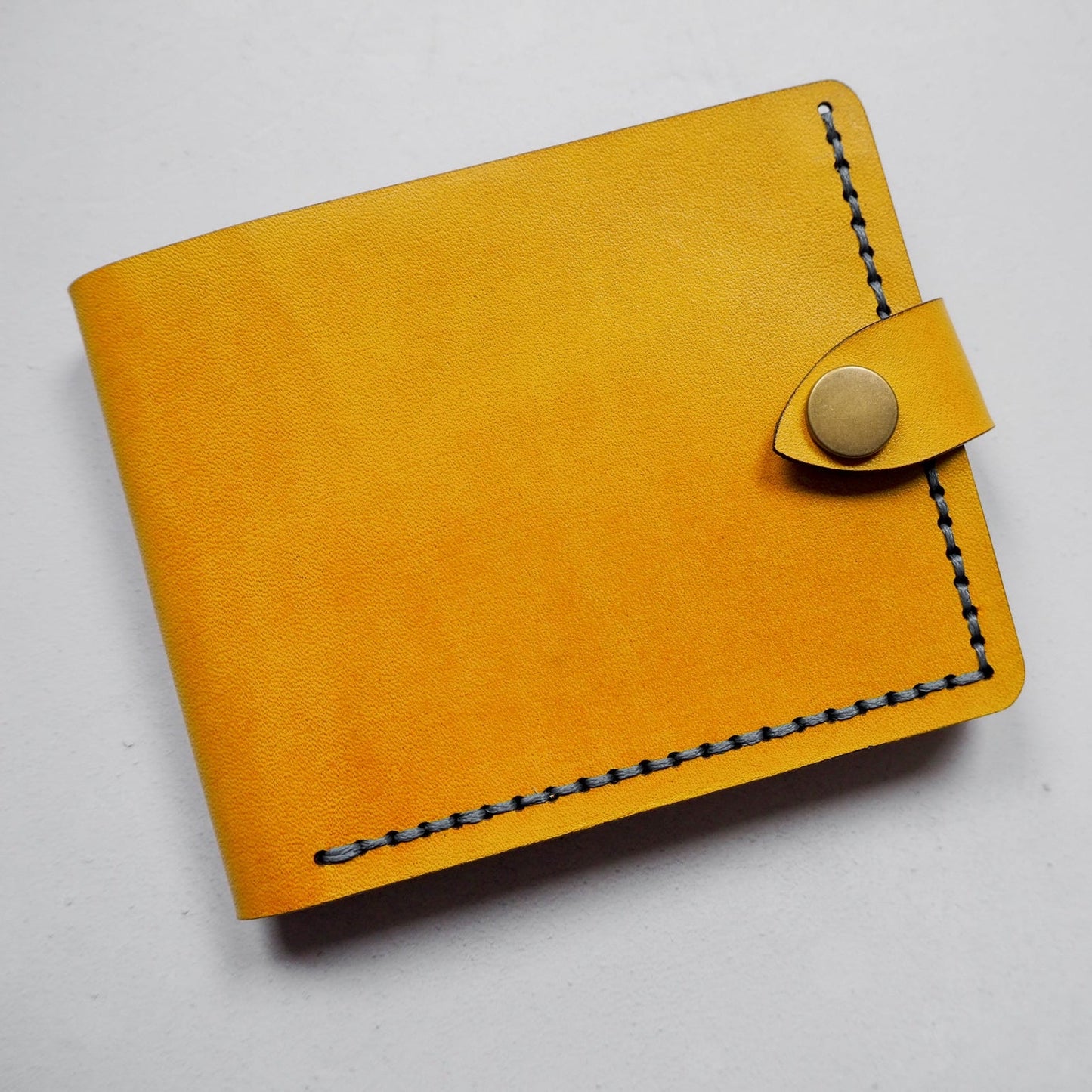 Yellow leather wallet with button closure on a white background