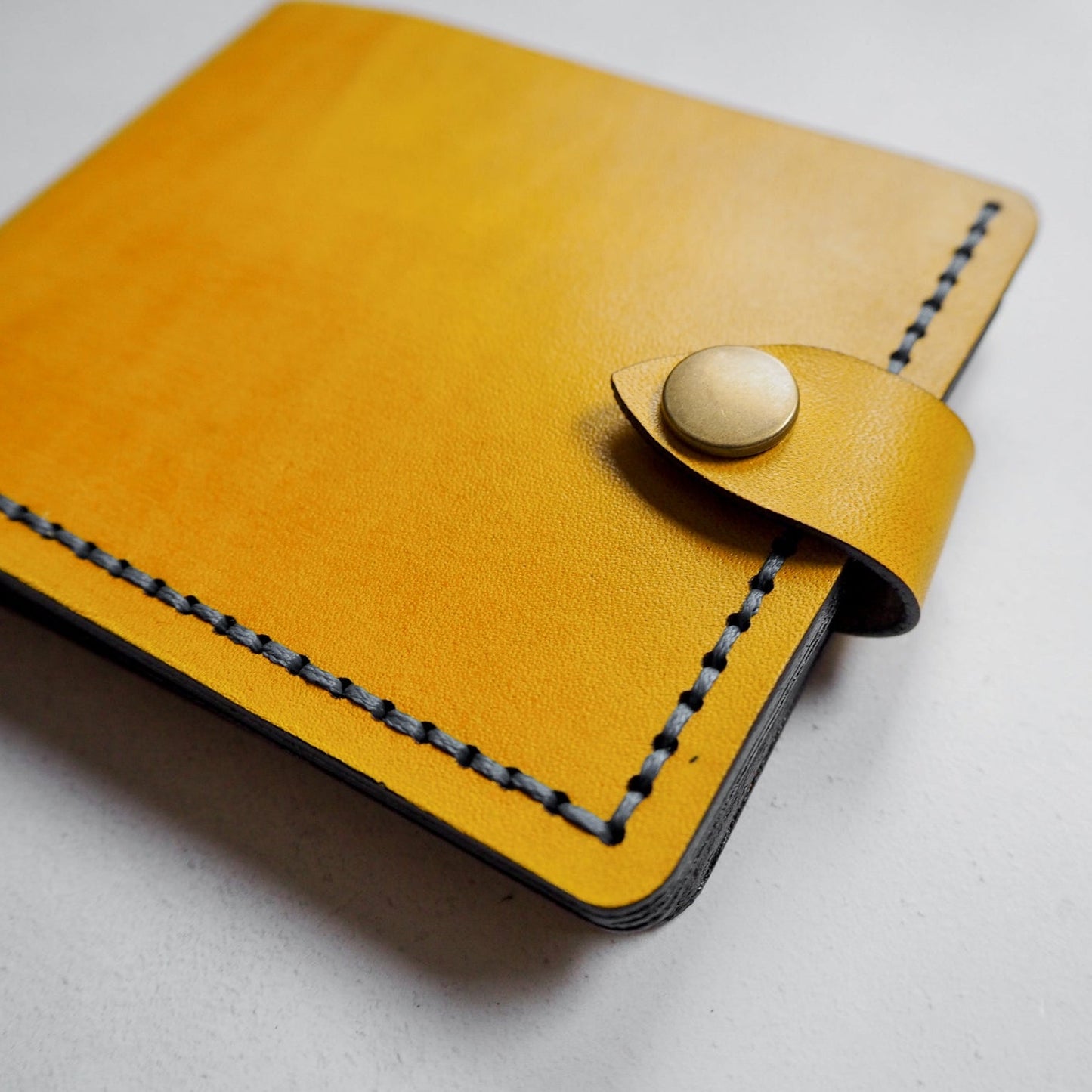 Yellow leather wallet with button closure on a light gray background