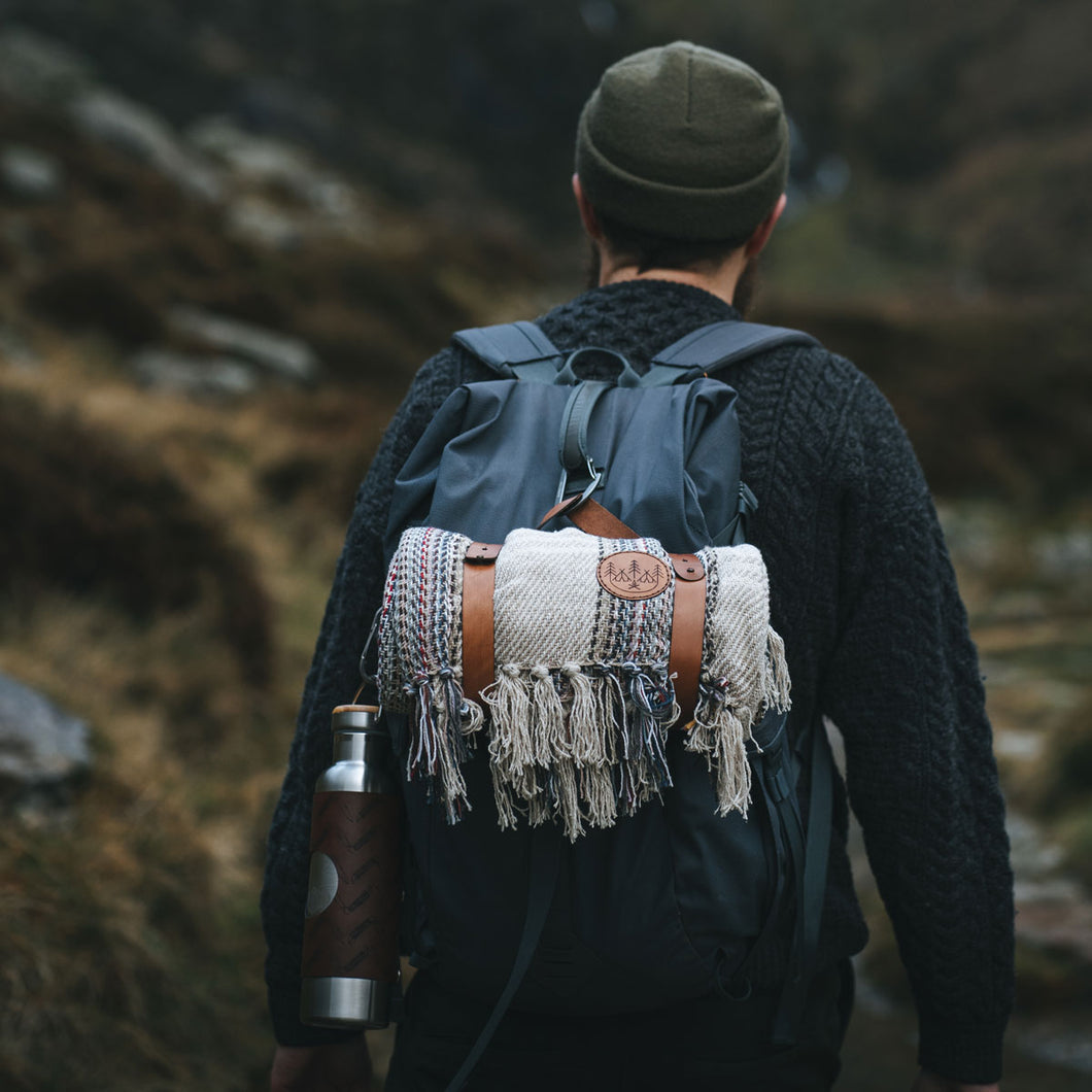  A person walking in the mountains of wales, with a rucksack that carries one of our recycled cotton blankets with blanket holder and our insulated water bottle. They wear our Olive green vegvisir beanie hat.
