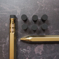 Gold pen and mechanical pencil with black erasers on a dark surface