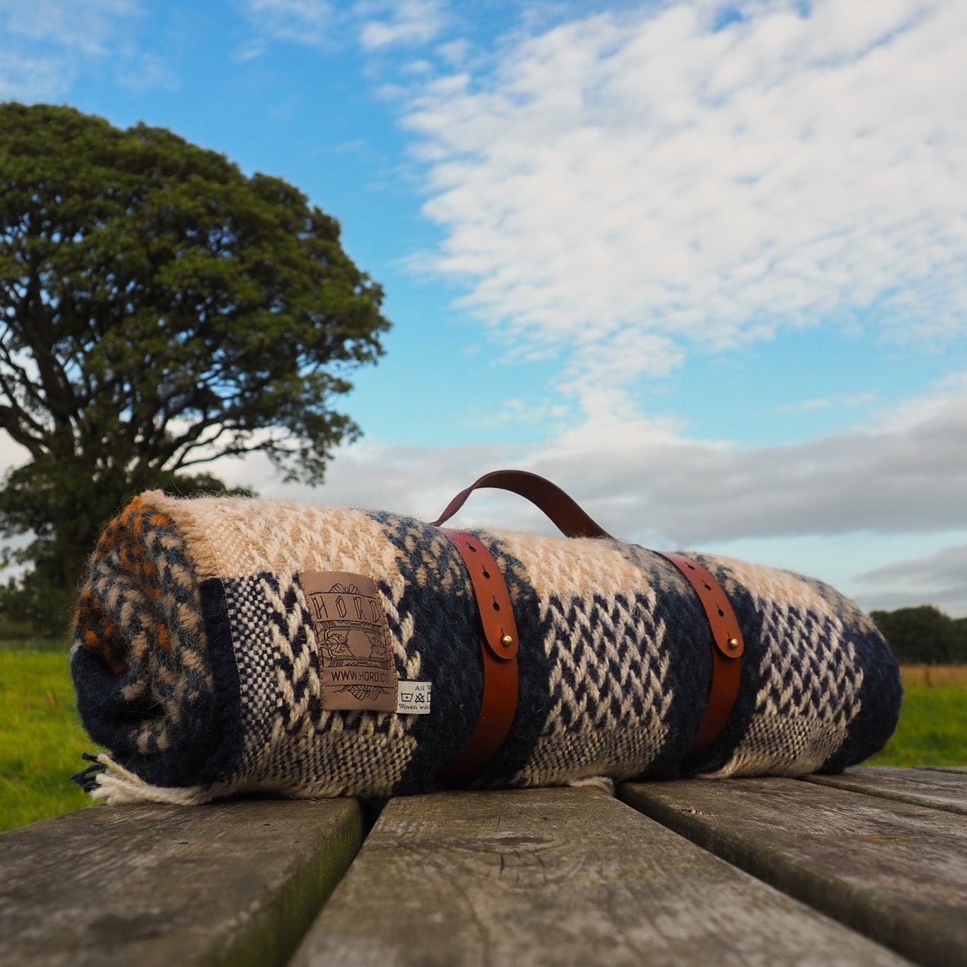 Roll-up blanket with patterned design on a wooden surface in a field with trees and blue sky.