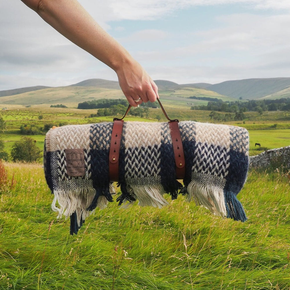 Person holding a patterned rug  in a grassy field with rolling hills in the background