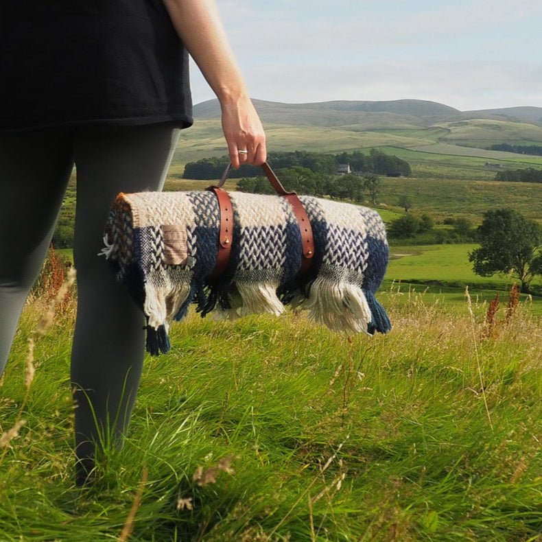Celtic Camper Blanket with Blanket Strap carried in a grassy field flanked by hills