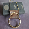 The antique brown Lunar Necklace is inspired by the phases of the moon, riveted leather remnants wrap over a solid ring. Perfect for adding a little ruggedness to your outfit. A lunar necklace by Hord.