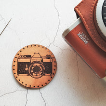  Circular leather patch in a tan patina engraved in black with the image of a vintage camera - pictured with a classic instax camera, a photographer patch from Hord.