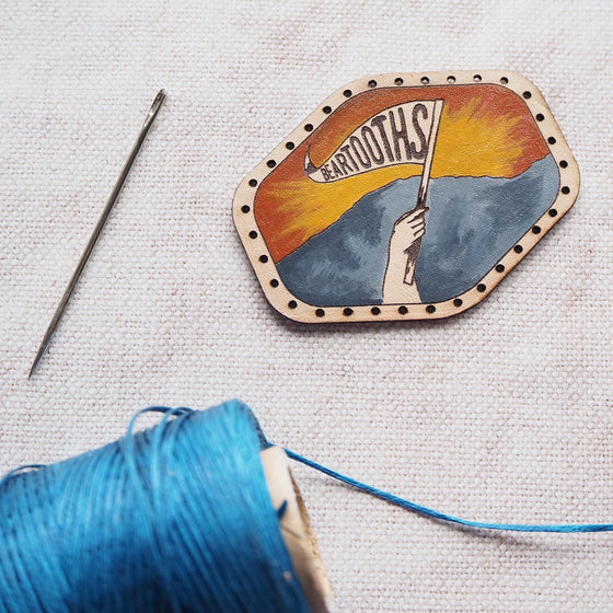 This leather patch features a hand painted mountain sunrise and a hand waving a flag with your choice of text - perhaps a recently conquered mountain name. The Hiking Patch from Hord.