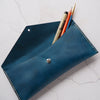 A personalised leather pencil case that has been hand dyed in blue with stationery stored inside.