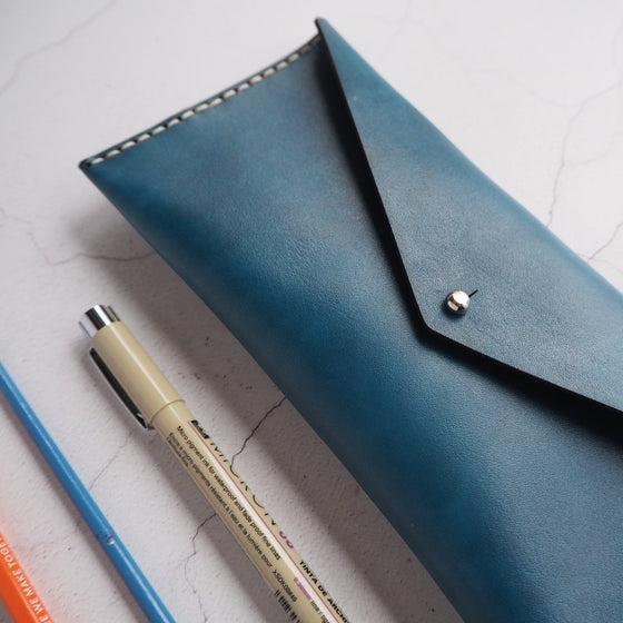 The Dyed Leather Pencil Case that has been hand dyed with blue leather colour and hand stitched with waxed white linen thread.