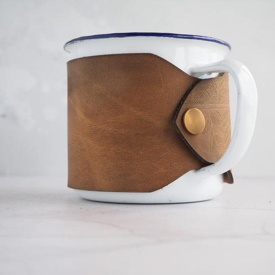 Camping enamel mug that's wrapped with leather featuring an illustration of fern leaves.