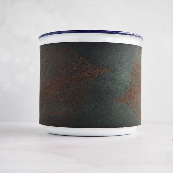 A camping enamel mug with a soft green leather wrap featuring a mulberry leaf engraving.
