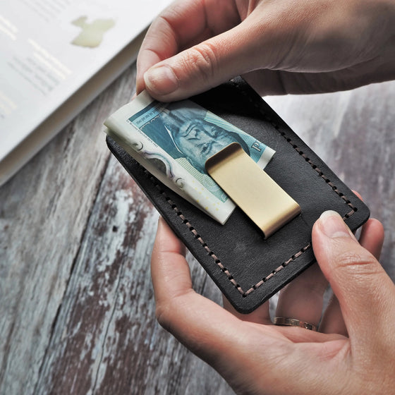 Cash being securely placed onto the money clip of the personalised leather card holder.