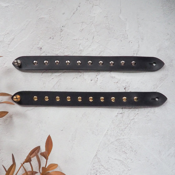 A black studded leather bracelet embedded with silver and brass studs.