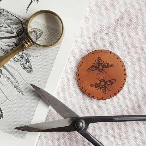 An illustration of two honey bees is engraved on this circular brown leather bee patch