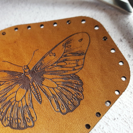 a close up of HORDs tan butterfly patch, showing the texture of the grain of the leather and the texture of the black surface engraving.