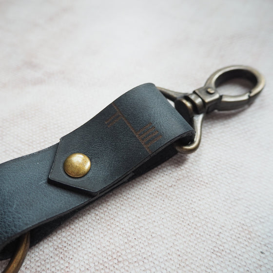 A personalised leather key fob with custom Ogham text and antique brass swivel material.